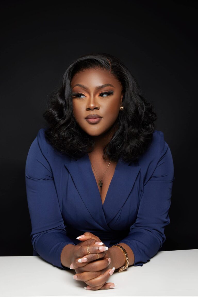 Professional headshot of a woman in a navy blazer against a dark backdrop